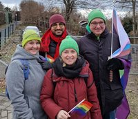 Bildbeschreibung; Gruppenbild: Antje Naumann, Kassem Taher Saleh (MdB), Berit Koch und Jens Bitzka (v.l.n.r) , Antje und Berit halten jeweils eine kleine Fahne in Regenbogenfarben, Jens hält eine große Fahne in Regenbogenfarben, Antje, Berit und Jens haben Grüne Mützen auf, Kassem trägt eine rote Mütze und einen roten Schal