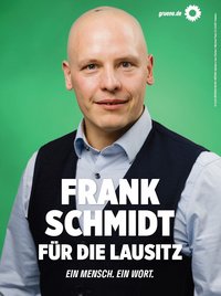 Bildbeschreibung:  Plakatmotiv mit Frank Schmidt, Hintergrund grün, oben rechts Sonnenblume und gruene.de, er hat eine dunkle Weste und ein helles Hemd an. Text: FRANK SCHMIDT FÜR DIE LAUSITZ EIN MENSCH. EIN WORT.