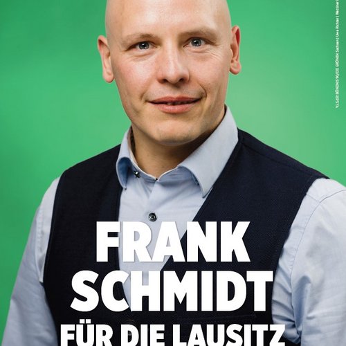 Bildbeschreibung: Plakatmotiv mit Frank Schmidt, Hintergrund grün, oben rechts Sonnenblume und gruene.de, er hat eine dunkle Weste und ein helles Hemd an. Text: FRANK SCHMIDT FÜR DIE LAUSITZ EIN MENSCH. EIN WORT.