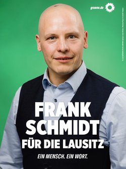 Bildbeschreibung:  Plakatmotiv mit Frank Schmidt, Hintergrund grün, oben rechts Sonnenblume und gruene.de, er hat eine dunkle Weste und ein helles Hemd an. Text: FRANK SCHMIDT FÜR DIE LAUSITZ EIN MENSCH. EIN WORT.