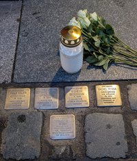 Fotobeschreibung 4 Stolpersteine auf dem Gehweg, 1 weiße Kerze, 9 liegende weiße Rosen