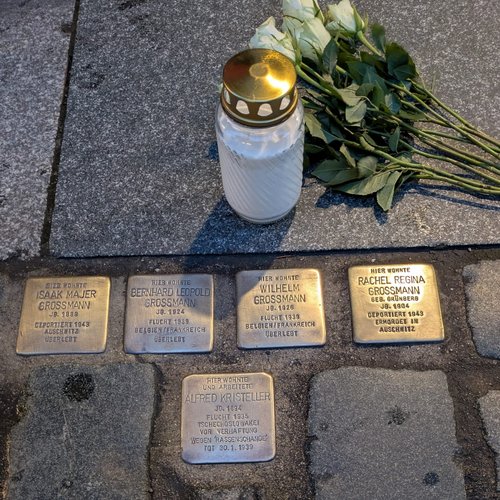 Fotobeschreibung 4 Stolpersteine auf dem Gehweg, 1 weiße Kerze, 9 liegende weiße Rosen