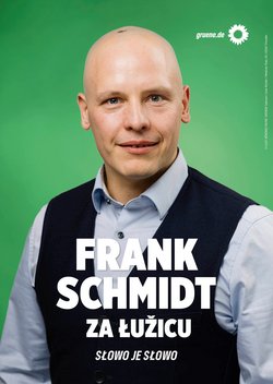 Bildbeschreibung:  Plakatmotiv mit Frank Schmidt, Hintergrund grün, oben rechts Sonnenblume und gruene.de, er hat eine dunkle Weste und ein helles Hemd an. Text: FRANK SCHMIDT ZA ŁUŽCU SŁOWO JE SŁOWO  
